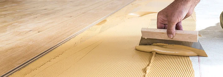 Person verteilt Kleber mit Spachtel auf Boden